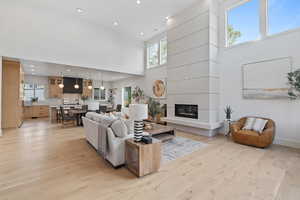 Living area with a towering ceiling, light wood-style floors, a large fireplace, and recessed lighting