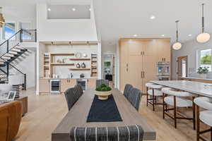 Dining space with beverage cooler, stairs, light wood-style floors, recessed lighting, and a high ceiling