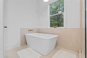 Full bath featuring a soaking tub and a wainscoted wall