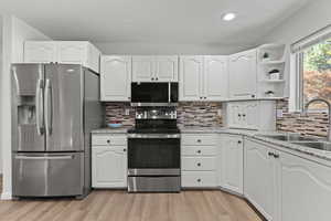 Kitchen featuring appliances with stainless steel finishes, white cabinets, open shelves, light wood-style flooring, and backsplash