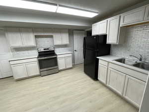 Kitchen featuring stainless steel electric range, freestanding refrigerator, decorative backsplash, light wood-style flooring, and white cabinets