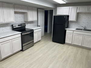 Kitchen with electric stove, freestanding refrigerator, tasteful backsplash, light wood finished floors, and light stone countertops