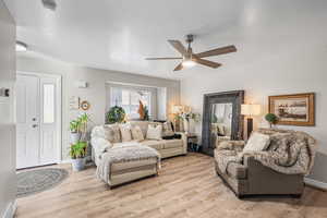 Living room featuring light wood finished floors, a textured ceiling, and ceiling fan
