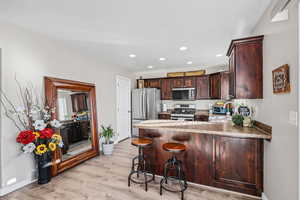 Kitchen with recessed lighting, dark brown cabinetry, a peninsula, stainless steel appliances, and a kitchen bar