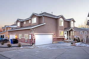 Traditional home featuring brick siding, stucco siding, driveway, and an attached garage