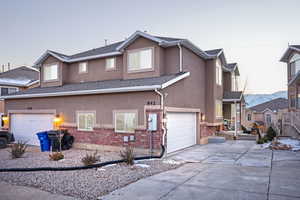 Traditional-style home featuring stucco siding, brick siding, driveway, and a garage
