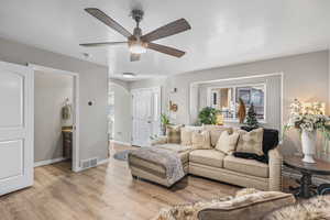 Living area with light wood finished floors, arched walkways, a textured ceiling, and a ceiling fan