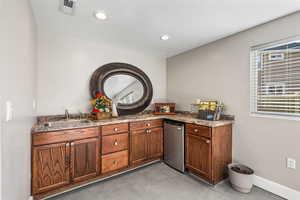 Indoor wet bar with finished concrete floors, stainless steel fridge, recessed lighting, and brown cabinets