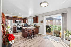 Kitchen with appliances with stainless steel finishes, a peninsula, a breakfast bar, light wood-type flooring, and dark brown cabinetry