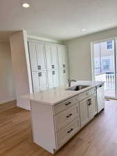 Kitchen featuring light stone countertops, an island with sink, light wood-style flooring, white cabinetry, and recessed lighting