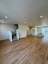 Unfurnished living room with a textured ceiling, light wood-type flooring, stairway, recessed lighting, and a chandelier