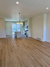 Unfurnished living room featuring a chandelier, light wood-style flooring, recessed lighting, and a textured ceiling