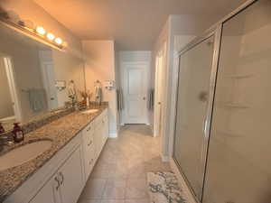 Bathroom featuring double vanity, a shower stall, and light tile patterned floors