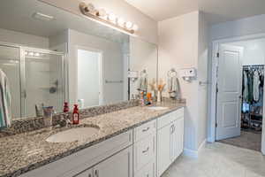 Full bathroom featuring double vanity, a stall shower, a walk in closet, and light tile patterned flooring