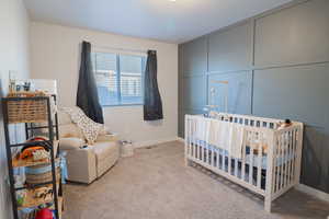 Bedroom featuring a crib, light carpet, and a decorative wall