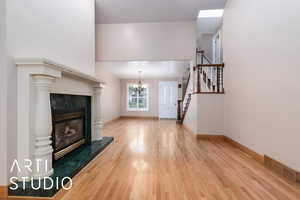Unfurnished living room featuring a tiled fireplace, light wood-style floors, stairs, and a chandelier