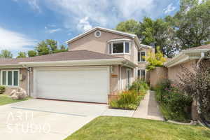 Traditional-style house with driveway, an attached garage, stucco siding, a front lawn, and roof with shingles