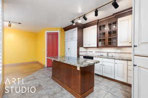 Kitchen with track lighting, light stone counters, white refrigerator with ice dispenser, and glass insert cabinets