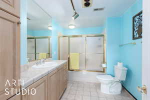 Full bathroom featuring vanity, enclosed tub / shower combo, rail lighting, and light tile patterned flooring