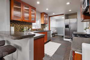 Kitchen featuring recessed lighting, appliances with stainless steel finishes, backsplash, glass insert cabinets, and a breakfast bar area