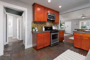 Kitchen featuring appliances with stainless steel finishes, dark countertops, tasteful backsplash, brown cabinetry, and stone tile floors