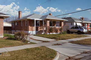 View of front of property featuring a front lawn, a chimney, brick siding, and roof with shingles