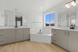 Bathroom with a stall shower, a bath, two vanities, and light wood finished floors