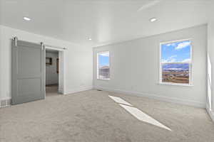 Unfurnished bedroom with a barn door, light colored carpet, and recessed lighting