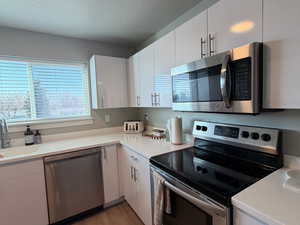 Kitchen featuring stainless steel appliances, white cabinetry, light wood finished floors, and a textured ceiling