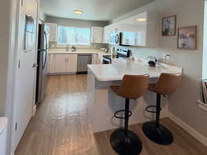Kitchen featuring white cabinets, light countertops, a kitchen breakfast bar, a peninsula, and appliances with stainless steel finishes