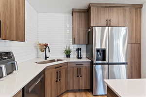 Kitchen featuring stainless steel appliances, light stone countertops, light wood finished floors, brown cabinetry, and a textured ceiling