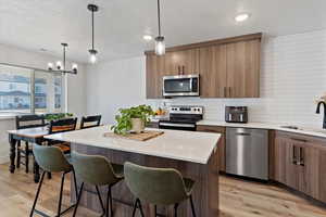 Kitchen with a kitchen island, decorative light fixtures, stainless steel appliances, decorative backsplash, and a textured ceiling