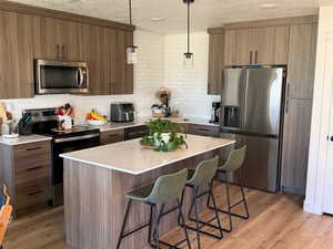 Kitchen with stainless steel appliances, a breakfast bar, a kitchen island, a textured ceiling, and light wood-style flooring