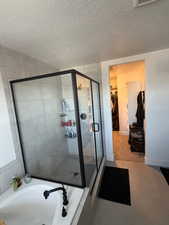 Bathroom with a spacious closet, a garden tub, a shower stall, a textured ceiling, and light tile patterned flooring