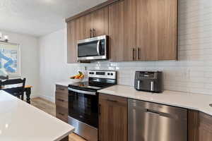 Kitchen featuring appliances with stainless steel finishes, modern cabinets, a textured ceiling, tasteful backsplash, and light wood-style floors