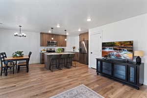 Kitchen with hanging light fixtures, a center island, a breakfast bar, stainless steel appliances, and light wood-style floors