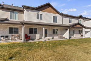 Rear view of property featuring board and batten siding, stone siding, a lawn, and covered porch