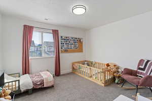 Carpeted bedroom with a nursery area and a textured ceiling
