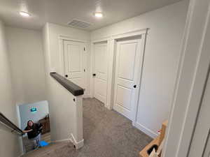 Hall featuring dark carpet, a textured ceiling, and an upstairs landing