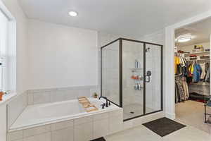 Full bath with a walk in closet, a bath, a stall shower, carpet, and tile patterned flooring