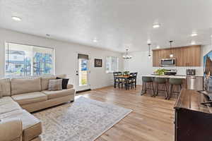 Living area featuring light wood-style floors, a chandelier, recessed lighting, and a textured ceiling
