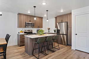 Kitchen featuring a breakfast bar, appliances with stainless steel finishes, hanging light fixtures, a kitchen island, and light wood-type flooring