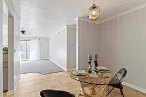 Dining space with ornamental molding, a textured ceiling, a ceiling fan, light colored carpet, and light tile patterned flooring