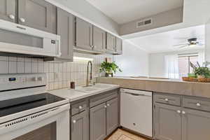 Kitchen featuring gray cabinets, white appliances, backsplash, light countertops, and a ceiling fan