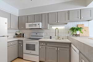 Kitchen with gray cabinets, white appliances, and backsplash