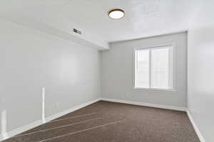 Empty room with dark colored carpet and a textured ceiling