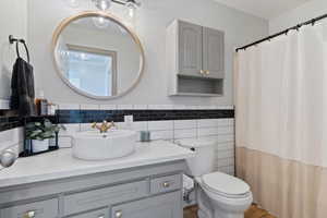 Bathroom featuring vanity, tile walls, curtained shower, and a wainscoted wall