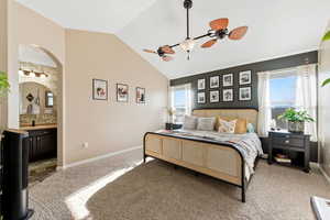Bedroom with arched walkways, vaulted ceiling, light colored carpet, multiple windows, and connected bathroom