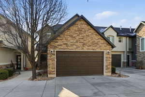 View of front of property featuring stone siding, driveway, stucco siding, and a garage