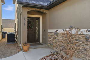 Doorway to property featuring stucco siding, stone siding, and a shingled roof